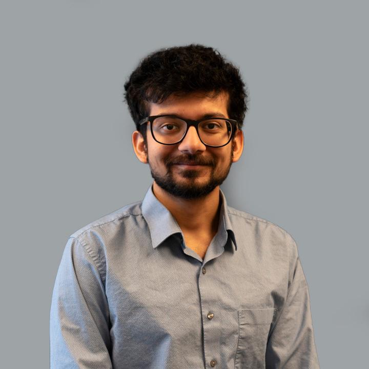 Lakshya Bharadwaj stands in front of a white background and smiles to the camera